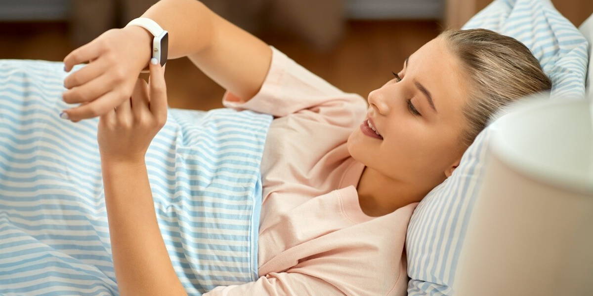 smiling girl with smart watch lying in bed at home