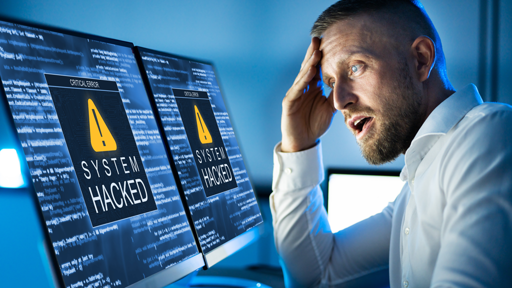 Man kijkt geschrokken naar computerscherm waar 'gehackt systeem' op staat