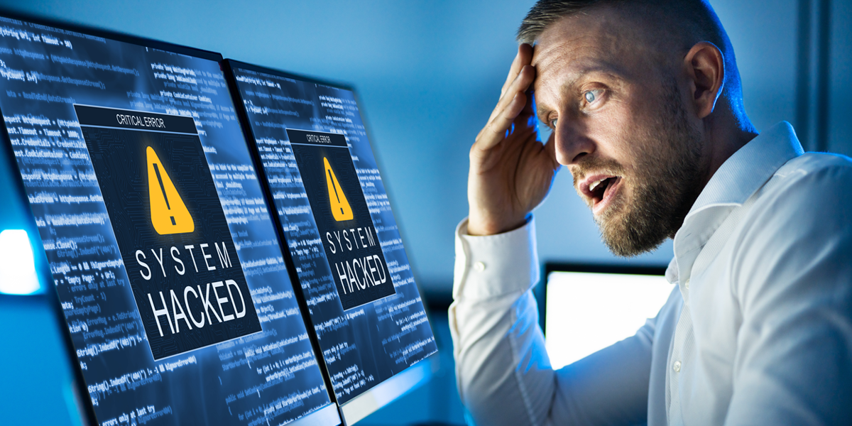 Man kijkt geschrokken naar computerscherm waar 'gehackt systeem' op staat