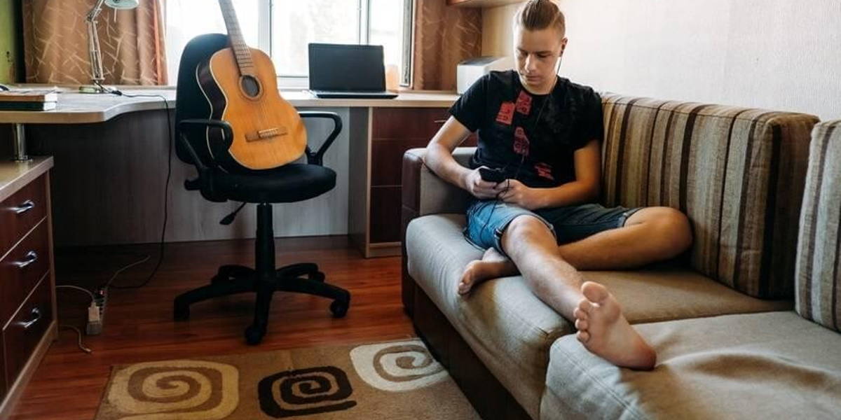 Digital Addiction in Tweens and Teens, smartphone addicted. Teenage boy playing online game, watching messengers in the smartphone laying on the couch at home