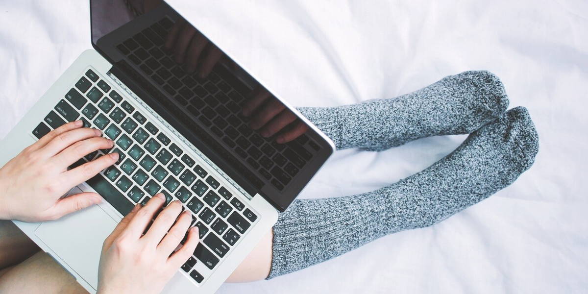 Top view of woman legs in socks and using laptop on cozy bed, li