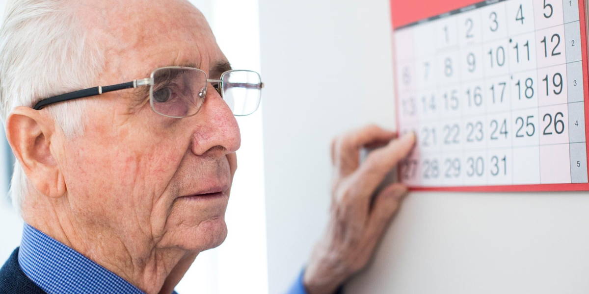 Confused Senior Man With Dementia Looking At Wall Calendar