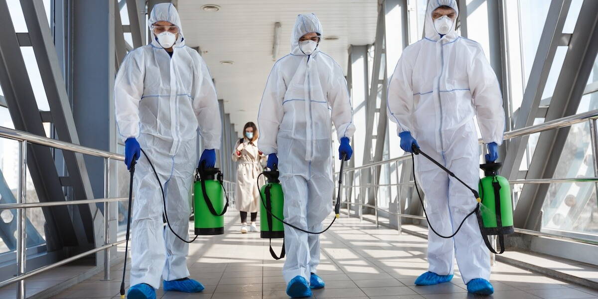 Drie mensen in een wit pak desinfecteren een ziekenhuisgang