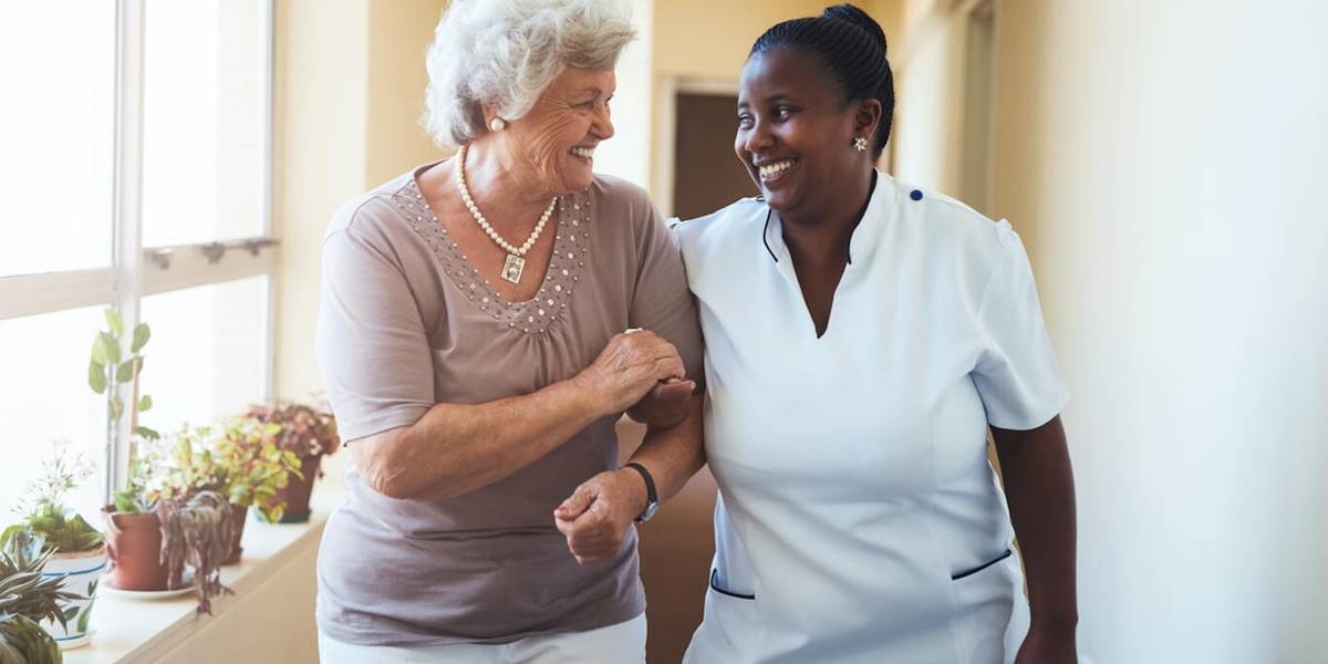 Smiling home caregiver and senior woman walking together