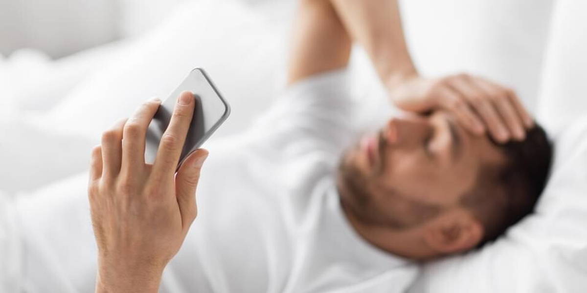 hand of young man with smartphone in bed