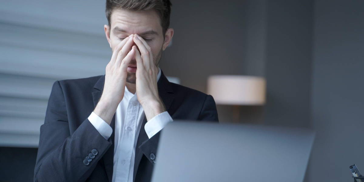 Overworked male entrepreneur sits at home office, suffering from heavy headache and fatigue