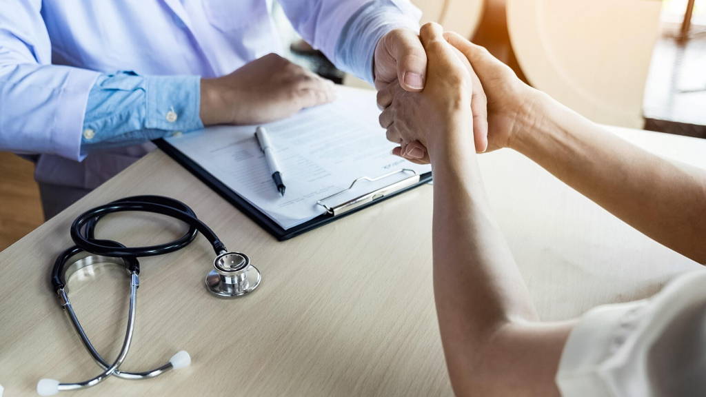 Doctor shakes hands at medical office with patient, wearing glas