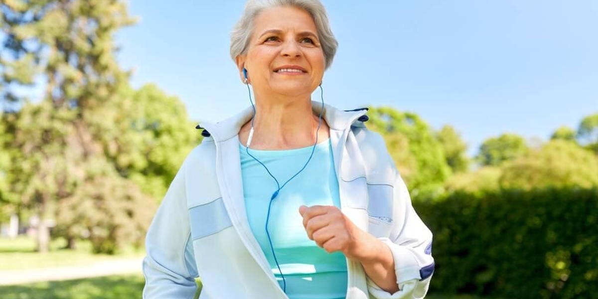 senior woman with earphones running in summer park
