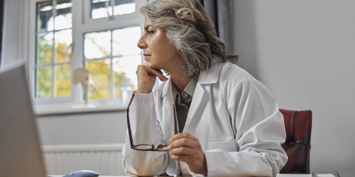 Stressed And Overworked Mature Female Doctor Wearing White Coat