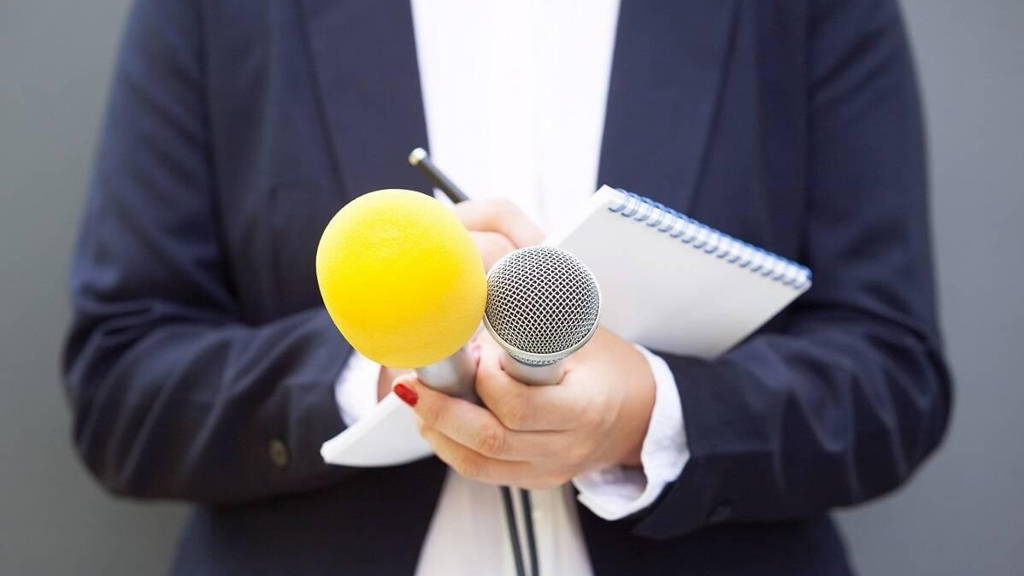 Journalist at news conference or media event, holding microphone and writing notes