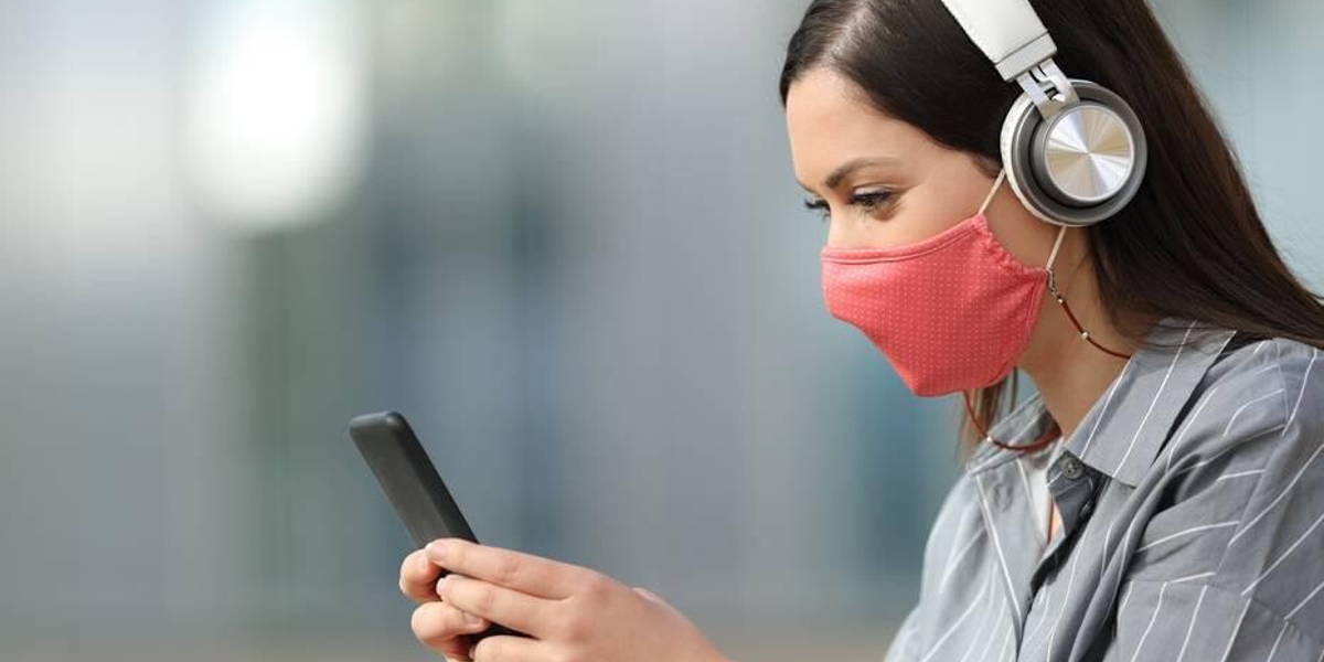 Woman with mask listening to music from smart phone