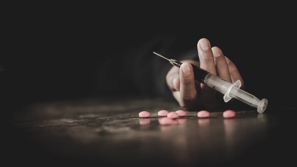 Hand met verslavende middelen: pillen en spuit