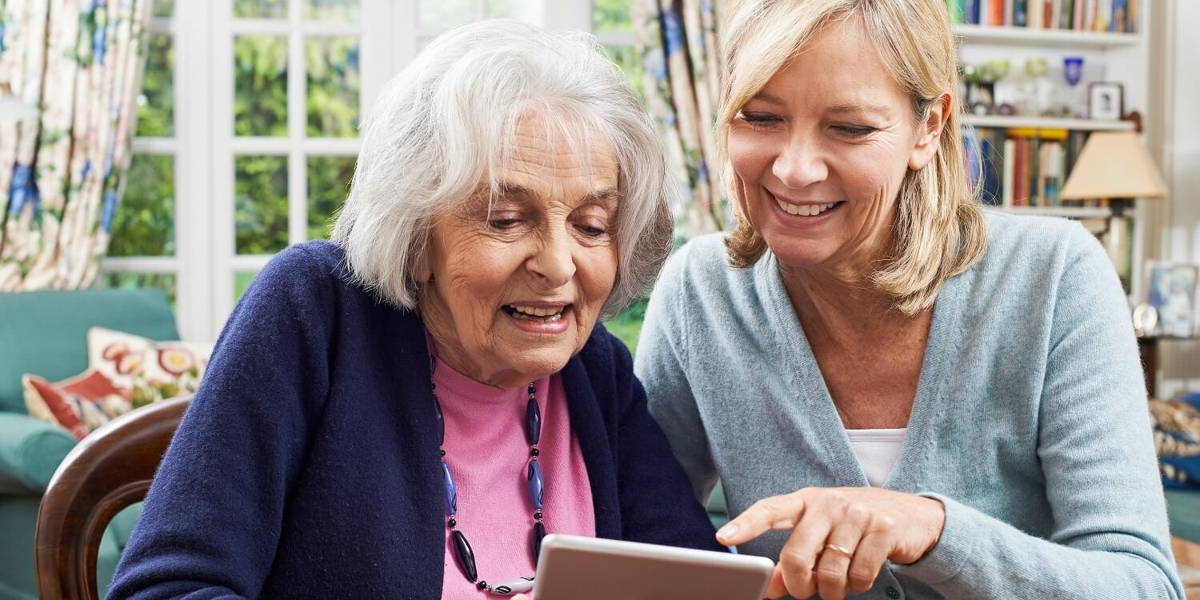 Female Neighbor Showing Senior Woman How To Use Digital Tablet