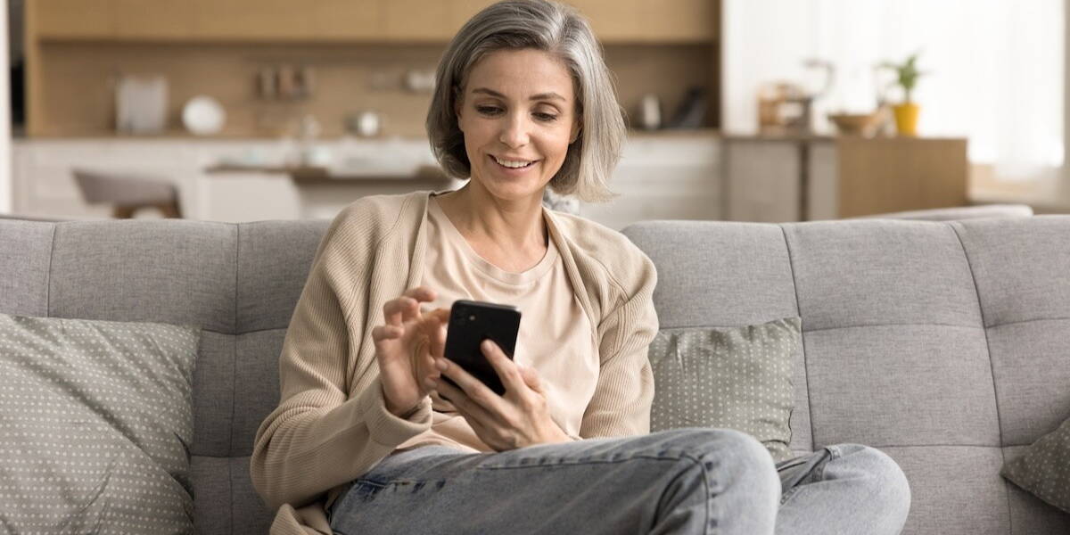 Lachende vrouw zit op een bank en kijkt naar haar smartphone