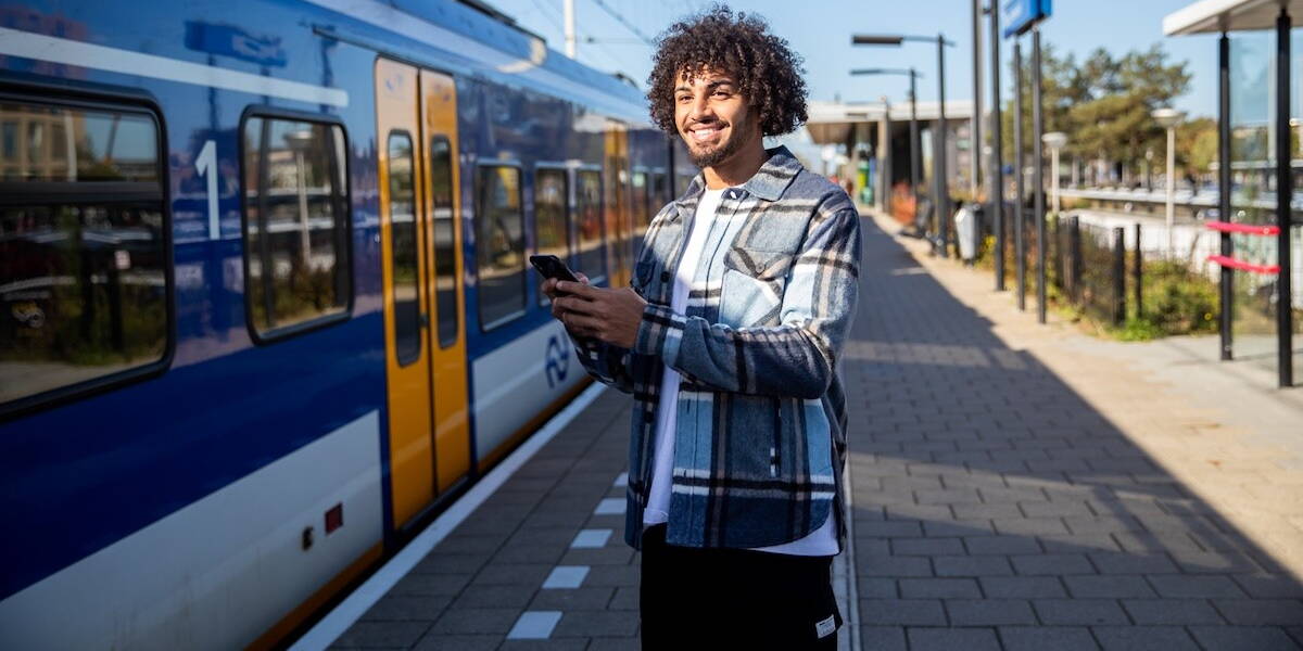 Man die met zijn smartphone in zijn hand voor een trein staat