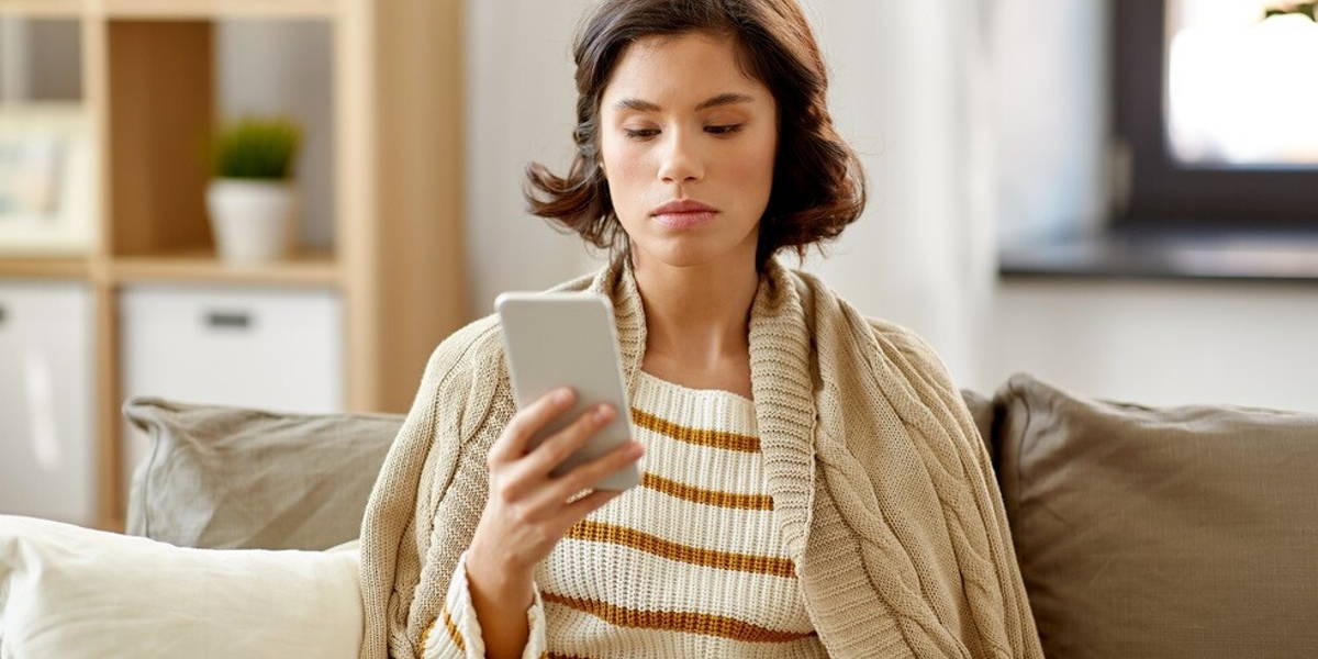 sad woman in blanket using smartphone at home