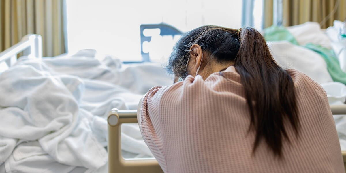 Vrouw zit moe naast ziekenhuisbed