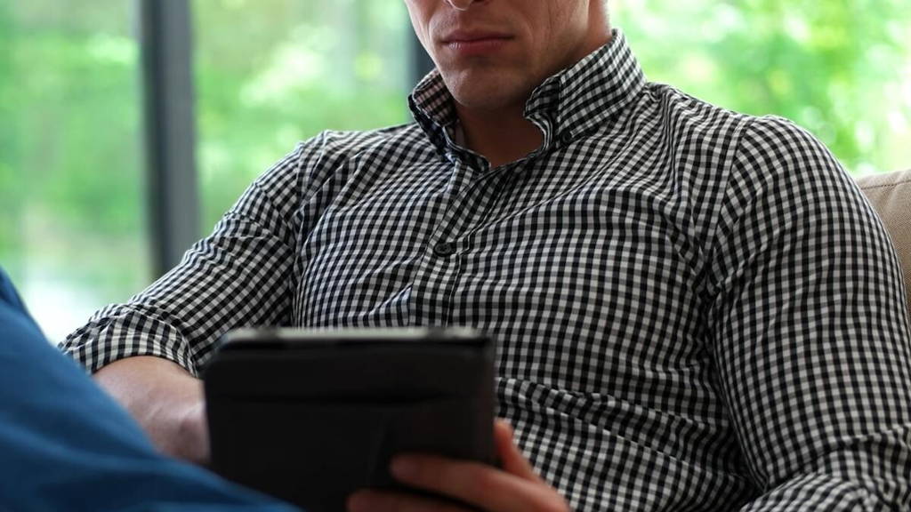 Man is Laying on Couch at Home and Using Tablet