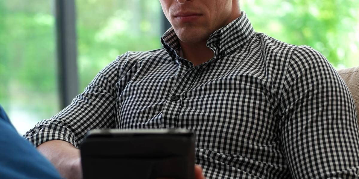 Man is Laying on Couch at Home and Using Tablet