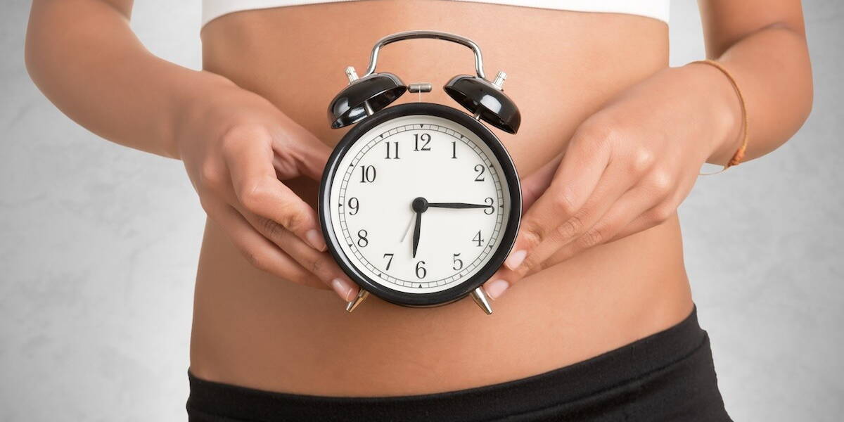 Vrouw houdt een klok voor haar buik.