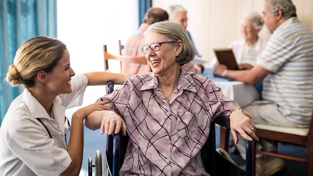Cheerful disabled senior woman sitting on wheelchair looking at female doctor