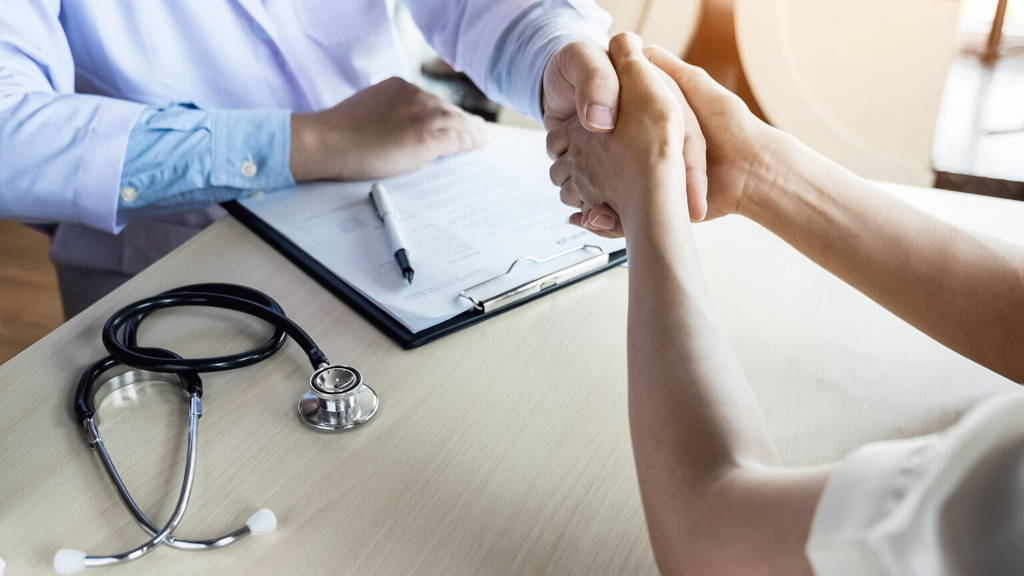Doctor shakes hands at medical office with patient, wearing glas