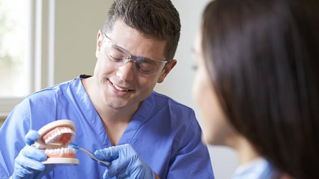 Dentist Demonstrating Correct Use Of Toothbrush To Female Client