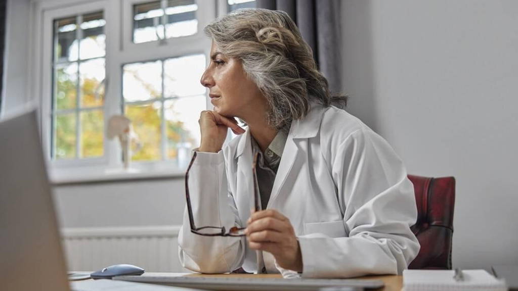 Stressed And Overworked Mature Female Doctor Wearing White Coat