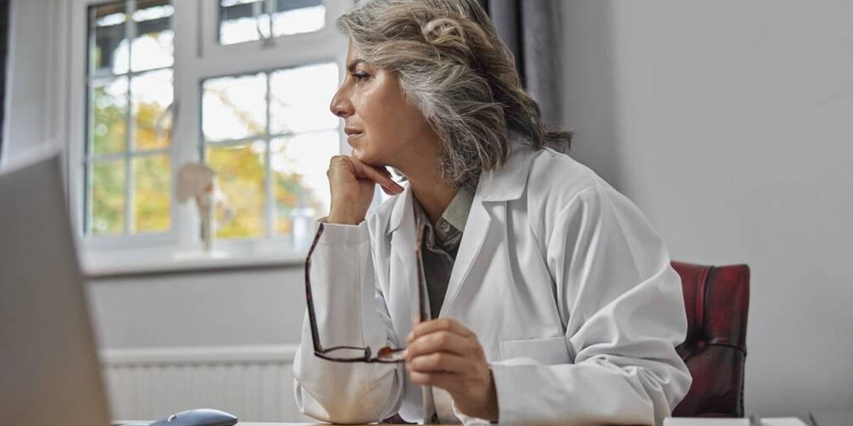 Stressed And Overworked Mature Female Doctor Wearing White Coat
