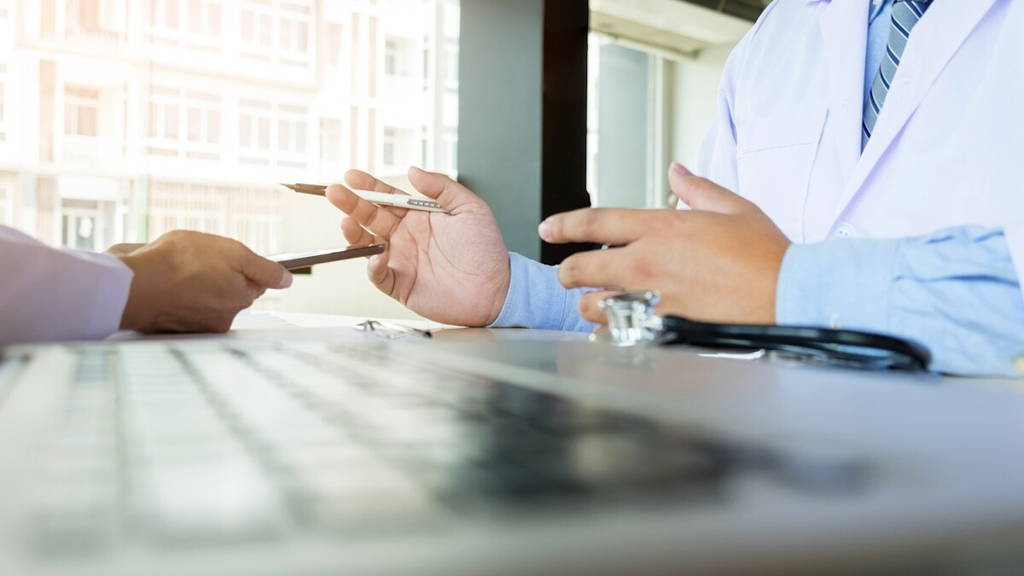 Two doctors discussing patient notes in an office pointing to a clipboard with tablet as they make a diagnosis or decide on treatment