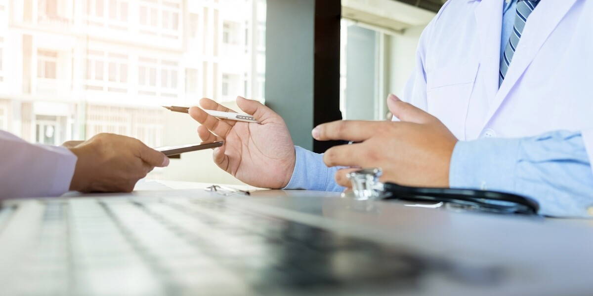 Two doctors discussing patient notes in an office pointing to a clipboard with tablet as they make a diagnosis or decide on treatment