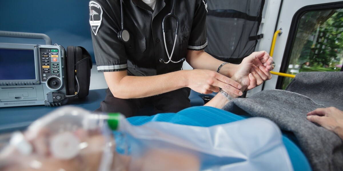 Ambulancemedewerker checkt de pols van een patiënt die op de brancard ligt