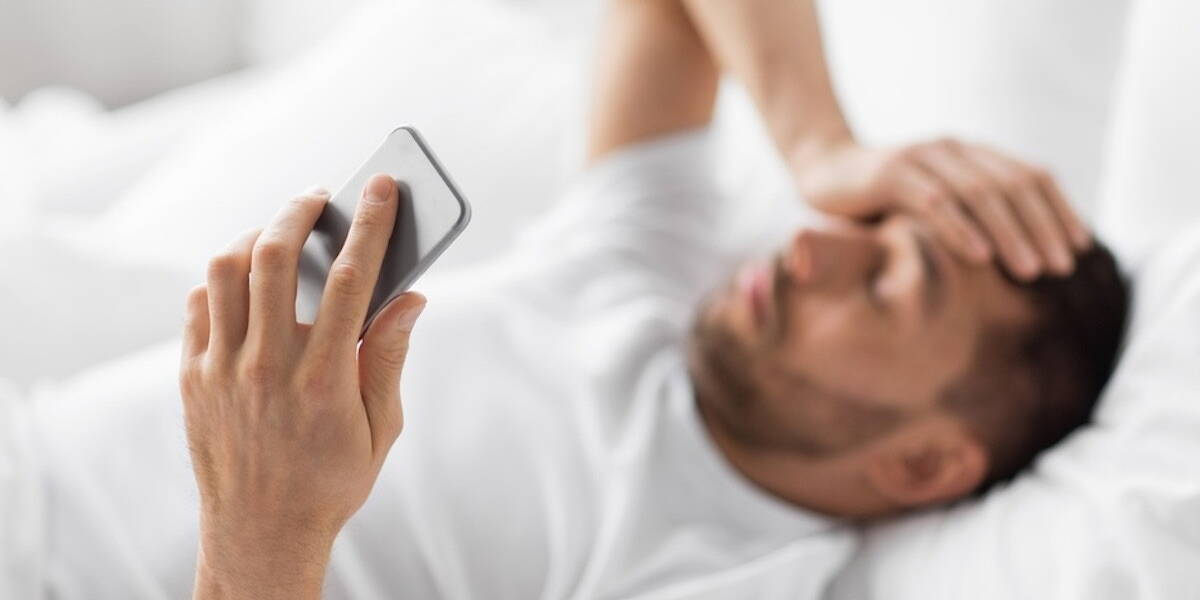 hand of young man with smartphone in bed