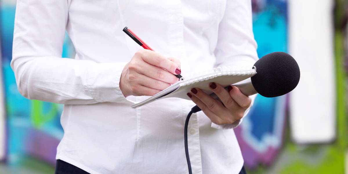 Female journalist at press conference, writing notes, holding mi